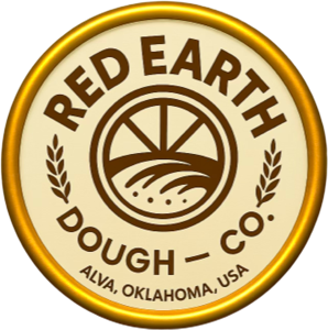 Red Earth Dough Co. circular company logo featuring stylized wheat fields and grain graphics representing agricultural roots, dough production, and food manufacturing. The logo includes the company name “Red Earth Dough Co.” and the location “Alva, Oklahoma, USA,” emphasizing American-made frozen pizza crust production, wheat-based food innovation, and commercial pizza manufacturing